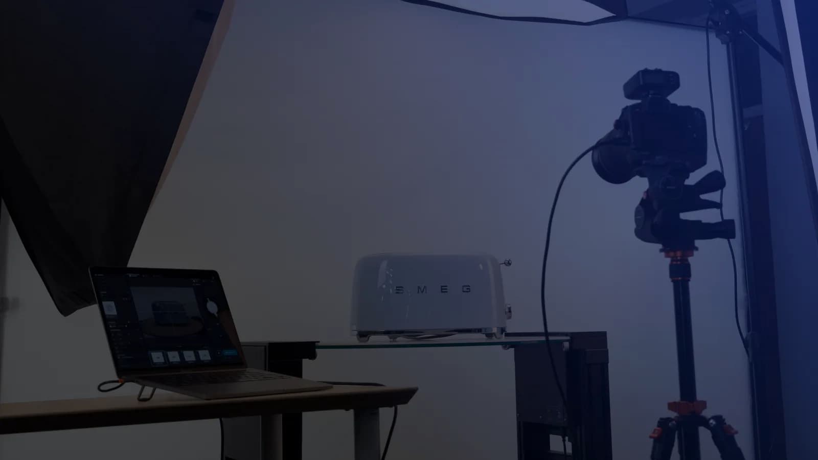 Stanowisko do fotografii produktowej z tetheringiem - laptop z oprogramowaniem obok aparatu na statywie i produktu na szklanej półce
