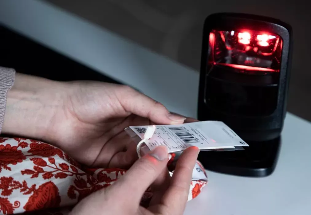Zbliżenie dłoni skanujących metkę odzieży z kodem kreskowym do inwentaryzacji